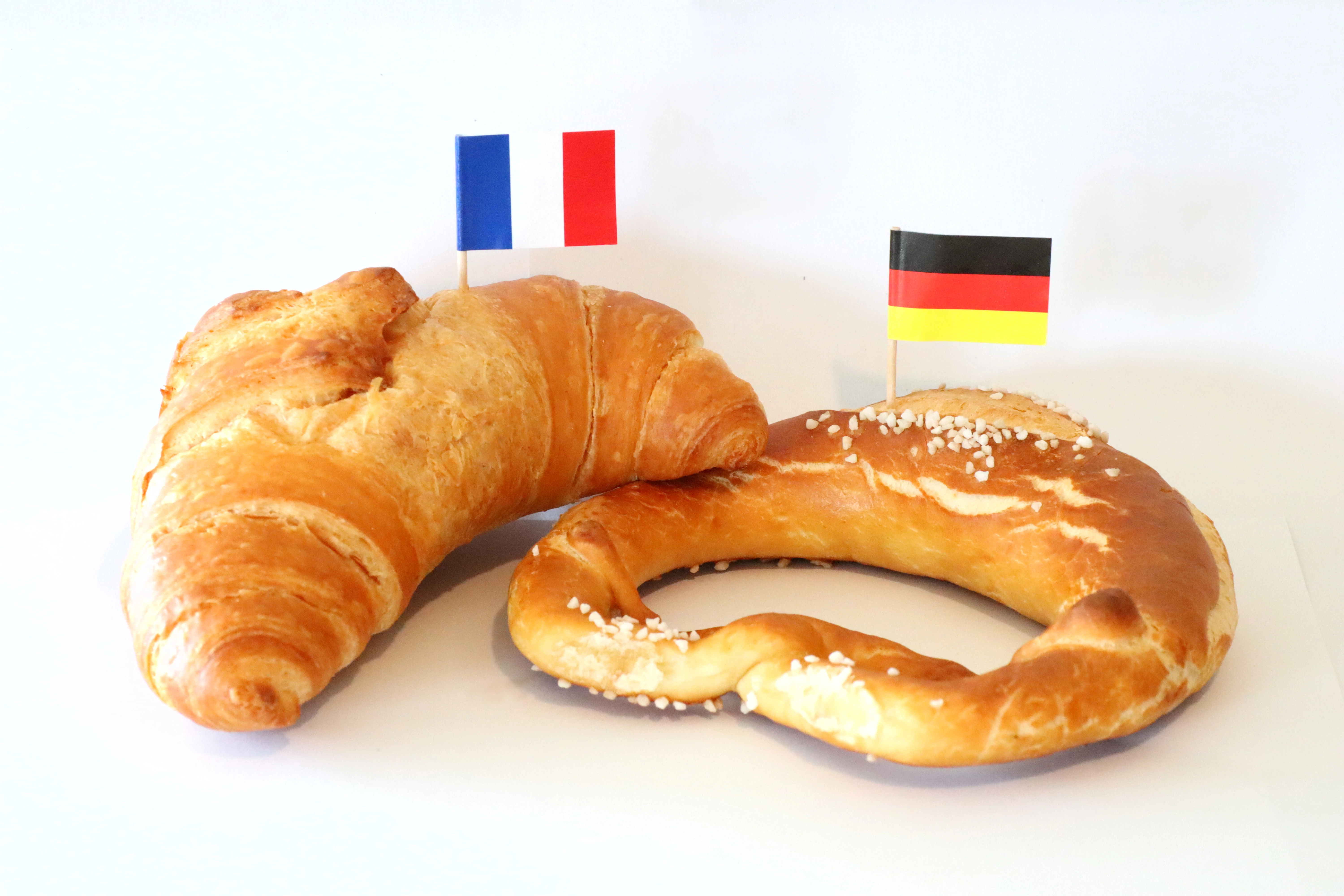 Ein Croissant mit einem Frankreich-Fähnchen neben einer Brezel mit einem Deutschland-Fähnchen