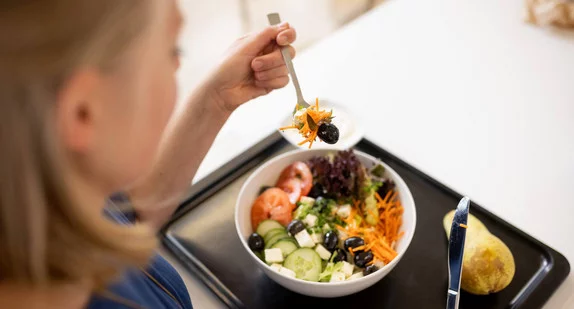 Eine Frau isst in einer Kantine einen bunten Salat.