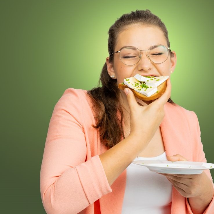 Eine junge Frau beißt mit geschlossenen Augen in ein Camembert-Brot.