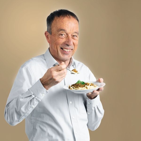 Ein älterer Mann isst lächelnd Linsen mit Spätzle.