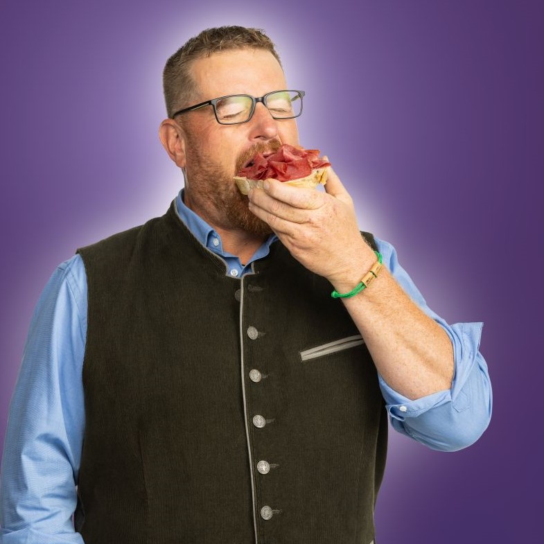 Ein Mann beißt herzhaft in ein mit Salami belegte Brötchenhälfte