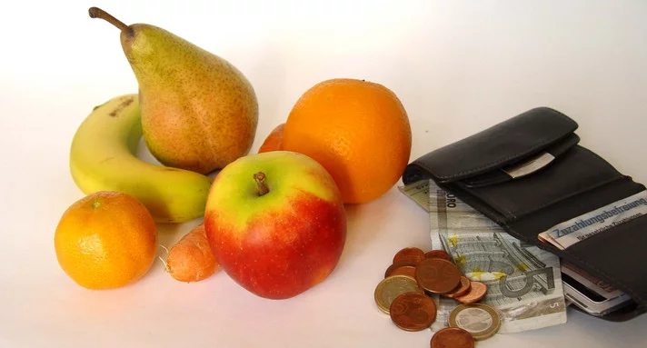 Neben Obst liegen ein geöffneter Geldbeutel und einige Münzen.