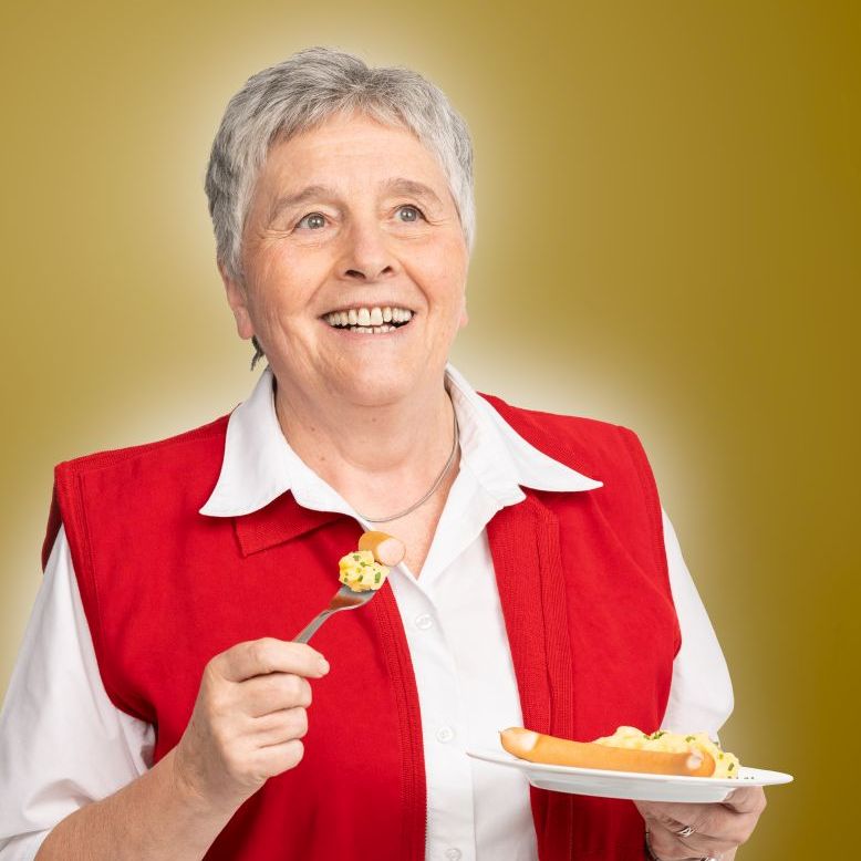 Eine ältere Frau isst genussvoll Kartoffelsalat mit Saitenwürstchen.